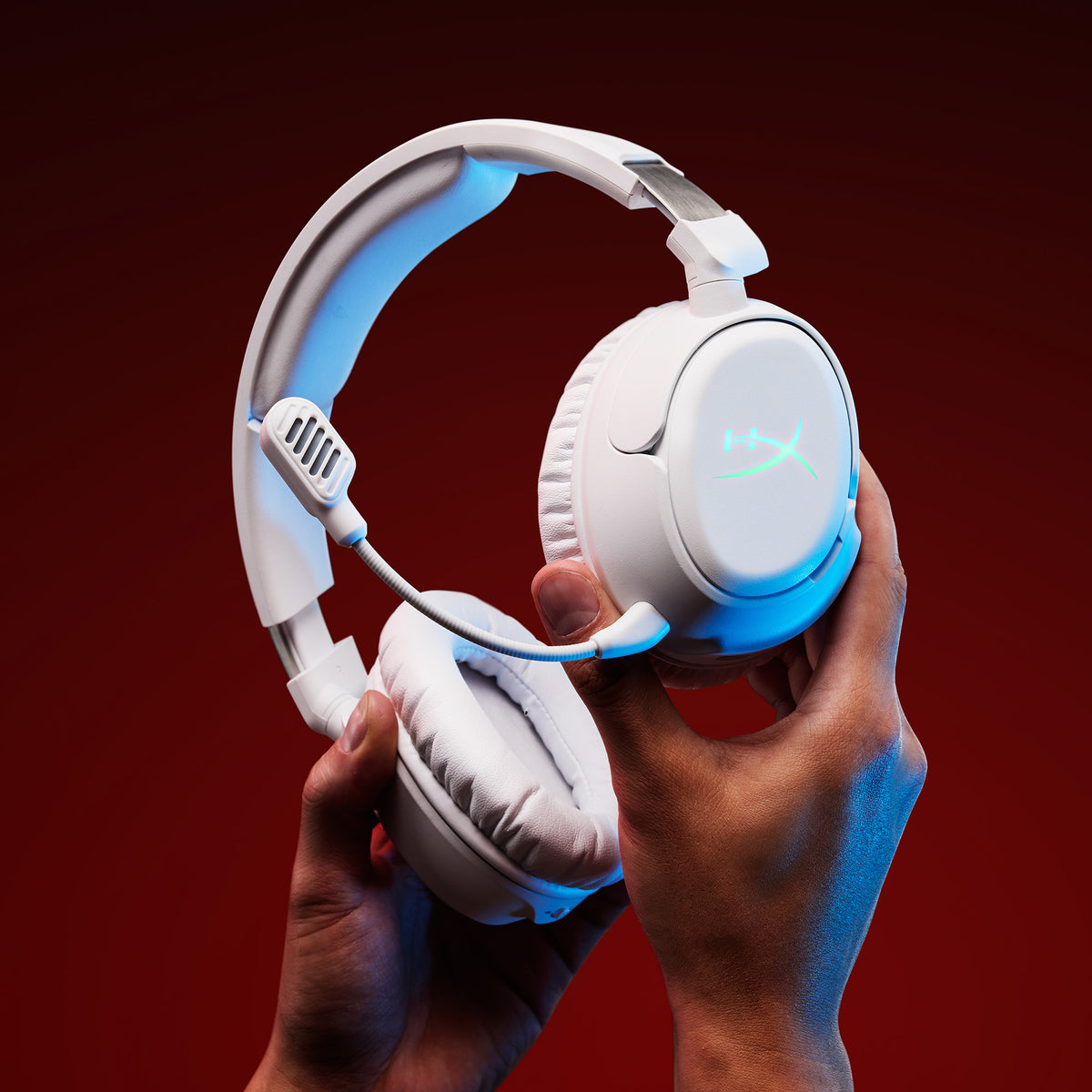 Beyaz HyperX Cloud Flight 2 kulaklığı iki elle tutan kullanıcı, kulaklık plakasında mavi aydınlatma